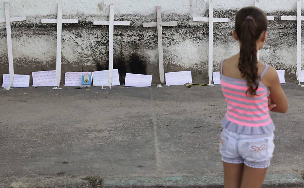 Menina olha cruzes e cartazes deixados em muro de escola no Rio após 12 mortes Leia Mais