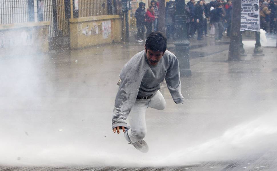 Estudantes chilenos fogem de jato d‘água lançado pela polícia durante protesto por melhorias no ensino, em Santiago