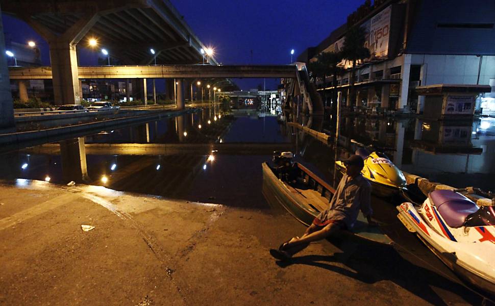 Morador de Bancoc, na Tailândia, senta-se em barco em área inundada, próximo a shopping