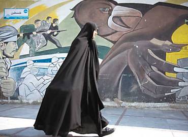 Em Teer, mulher passa em frente a painel de vis nacionalista; exaltaes  grandeza do pas fazem parte do mobilirio urbano na capital iraniana