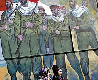 Em Teer, mulheres passam por mural que retrata soldados iranianos na Guerra Ir-Iraque