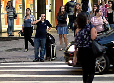 Pedestre fala ao celular no cruzamento da av. Paulista com a rua Frei Caneca