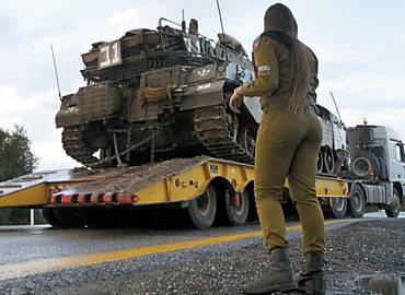 Uma militar observa caminhão deslocando tanque de guerra de Israel nas colinas do Golã