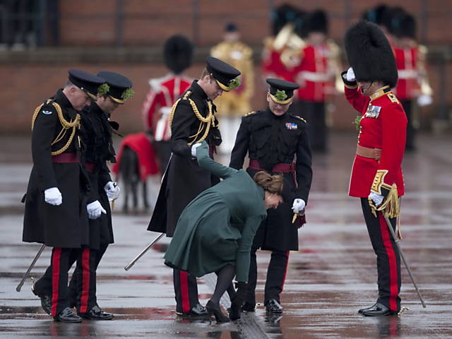 Príncipe William (à esq.) ajuda Kate Middleton a tirar o salto dela, que enganchou em um buraco, em uma visita a Aldershot, no sul da Inglaterra, no Dia de São Patrício