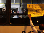 Manifestante mostra cartaz para passageiros dentro de ônibus; manifestação terminou com vários feridos
