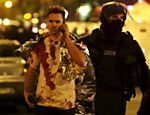 Policial acompanha homem com a roupa suja de sangue nas imediação da casa de shows parisiense Bataclan, onde várias pessoas foram mortas em um ataque terrorista