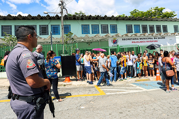 Policial militar diante do posto de saúde de Mairiporã lotado devido à busca por vacina
