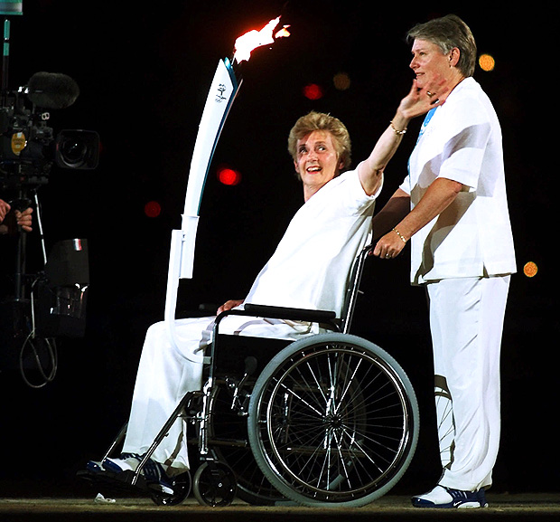 FILE - In this file photo dated Friday, Sept. 15, 2000, the 1956 sprint champion Betty Cuthbert who is confined to a wheelchair with Multiple Sclerosis, waves as she is pushed by three-time silver medal winner Raelene Boyle as they carry the Olympic torch during the opening ceremony of the 2000 Olympics in Sydney. Betty Cuthbert, the only runner to win Olympic gold medals in the 100-, 200- and 400-meter sprints, has died in Western Australia, aged 79, following a long battle with multiple sclerosis, according to a statement issued by Athletics Australia, Monday Aug. 7, 2017. (AP Photo/David Guttenfelder, FILE) ORG XMIT: LON106
