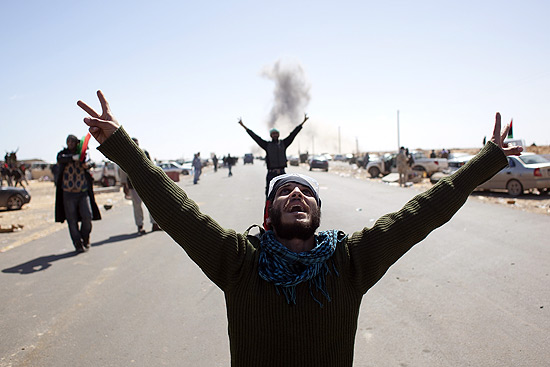 Rebeldes fazem sinal da vitória olhando para um avião que jogou bomba contra a cidade de Ras Lanuf