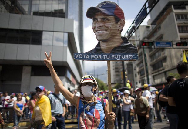 A woman holds up a banner with the image of Venezuelan opposition leader Henrique Capriles as people gather for a demonstration against President Nicolas Maduro in Caracas, Venezuela, Saturday, April 8, 2017. Capriles was banned from running for office for 15 years. Opponents of President Nicolas Maduro are preparing to flood the streets of Caracas on Saturday as part of a week-long protest movement that shows little sign of losing steam. (AP Photo/Ariana Cubillos) ORG XMIT: XAC101
