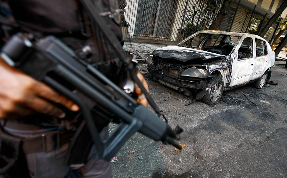 Policial observa carro incendiado de madrugada na rua Jornalista Orlando Dantas, em Botafogo, na zona sul do Rio <b>