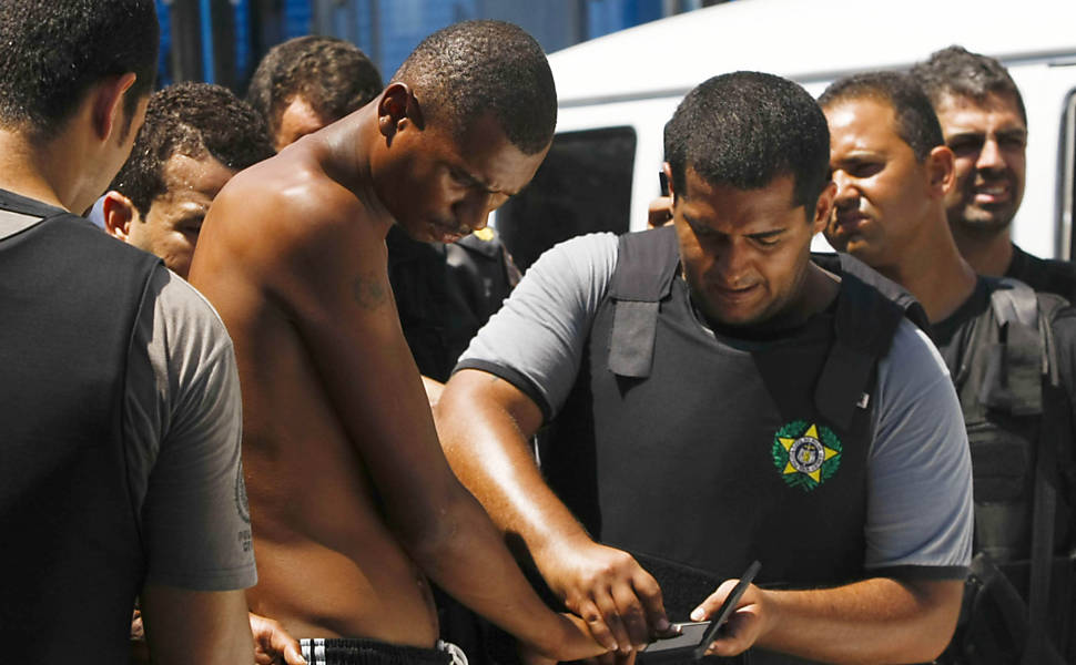 Policial recolhe digitais de morador do Complexo do Alemão, conjunto de favelas na zona norte do Rio <b>