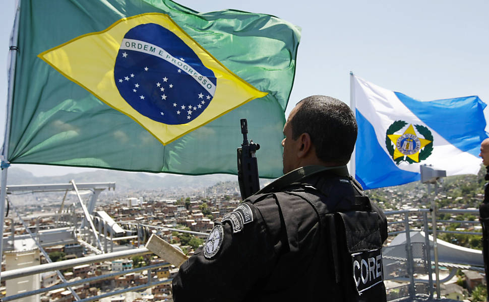 Policiais hasteiam a bandeira do Brasil e da Polícia Civil fluminense no alto da futura estação de um teleférico no Complexo do Alemão, conjunto de favelas na zona norte do Rio <b>