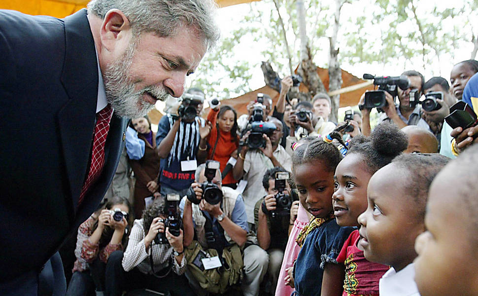 Texto: O presidente Luiz Inácio Lula da Silva (esq.) conversa com crianças durante visita ao Hospital Central de Maputo, em Moçambique. Lula participou de uma doação simbólica de medicamentos conta a Aids para o país africano, onde 13% da população adulta tem o vírus HIV. O Brasil integra o combate à Aids em Moçambique desde 2000, no governo de Fernando Henrique Cardoso. (Brazilian President Luiz Inacio Lula da Silva speaks with Mozambican children during a visit to the Central Hospital in Maputo, November 6, 2003. Lula attended the inauguration of a joint program to treat AIDS patients. (NO SALES) REUTERS/HO-Ricardo Stuckert/Brazilian Presidency)
