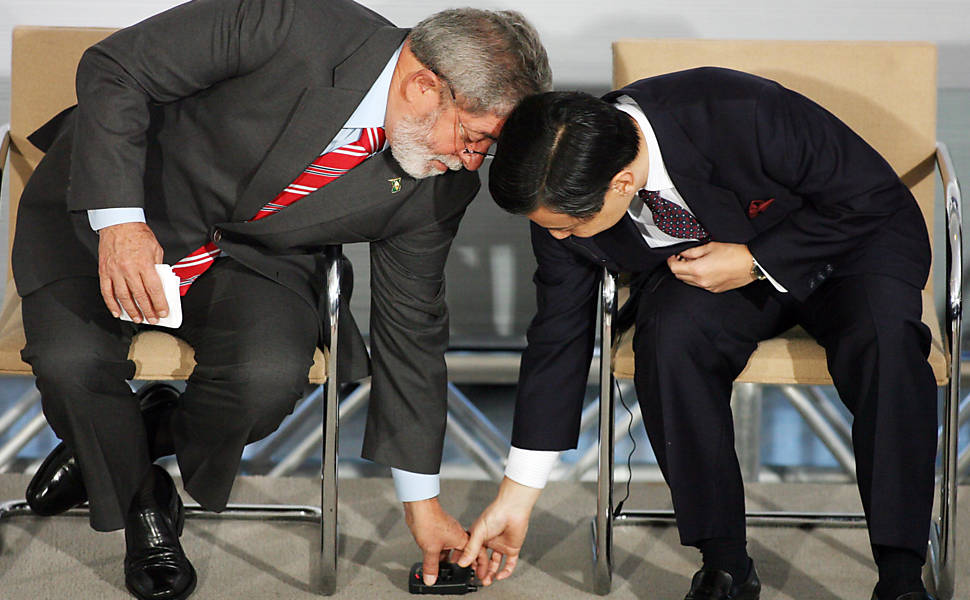 O presidente da República, Luiz Inácio Lula da Silva (à esq.) e o príncipe herdeiro do trono japonês, Naruhito Kotaishi, se abaixam para pegar equipamento de tradução durante cerimônia sobre a imigração japonesa, no Palácio do Planalto, em Brasília (DF)