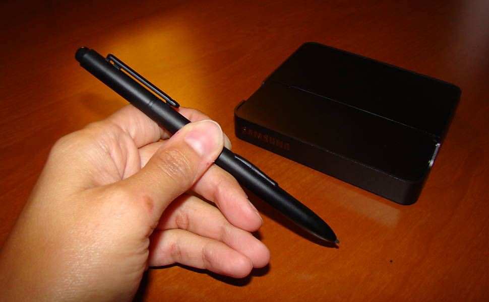 Caneta para usar a tela sensível ao toque do tablet da Samsung; atrás, o dock do aparelho Leia Mais