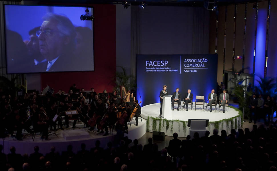 Dilma faz afagos ao novo ministro durante evento na Associação Comercial; Afif (no telão) estava na primeira fila da plateia 