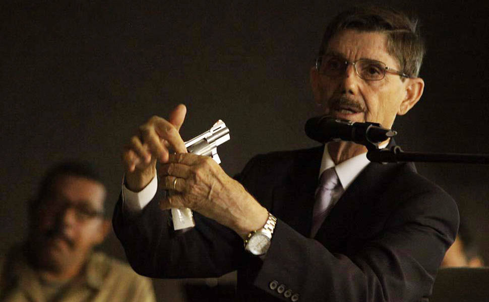 Perito Domingos Tochetto empunha arma para demonstrar trajetória da bala no corpo de Suzana Marcolino