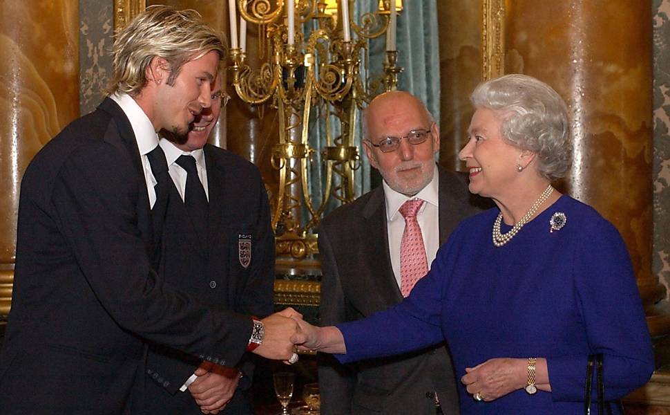 Em foto de 2002, a rainha da Inglaterra, Elizabeth 2ª, cumprimenta o jogador de futebol britânico David Beckham, em Londres