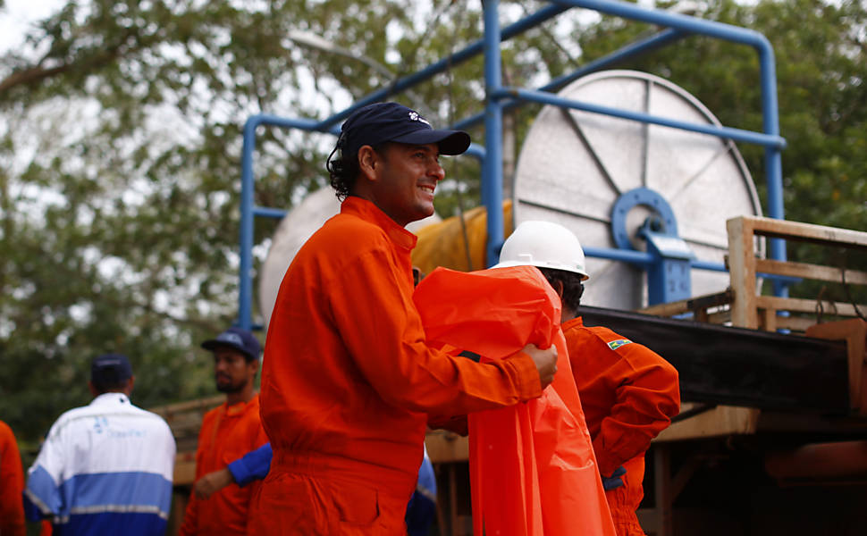 Operários trabalham para abrir vala para auxiliar lama de rio escoar no mar