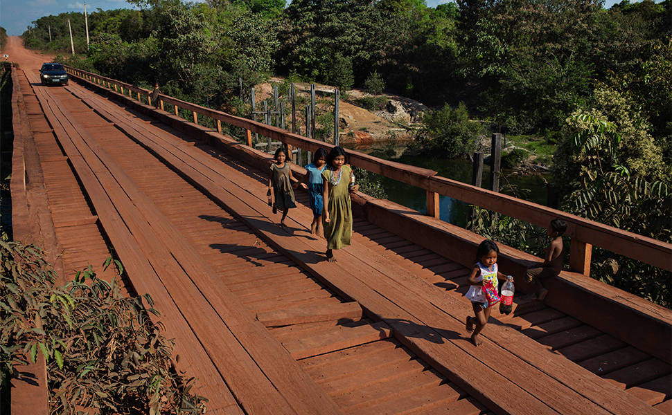 Crianças pirahãs atravessam ponte sobre o rio Maici na rodovia Transamazônica carregando sacos de salgadinhos obtidos com os viajantes que passam pelo local