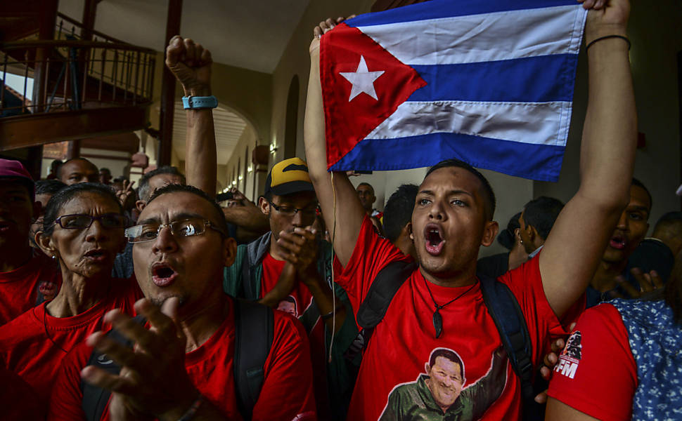 Apoiadores do presidente venezuelano Nicolas Maduro acenam com bandeiras de Cuba em frente a imagem de Hugo Chavez, durante cerimônia de homenagem a Fidel Castro em Caracas