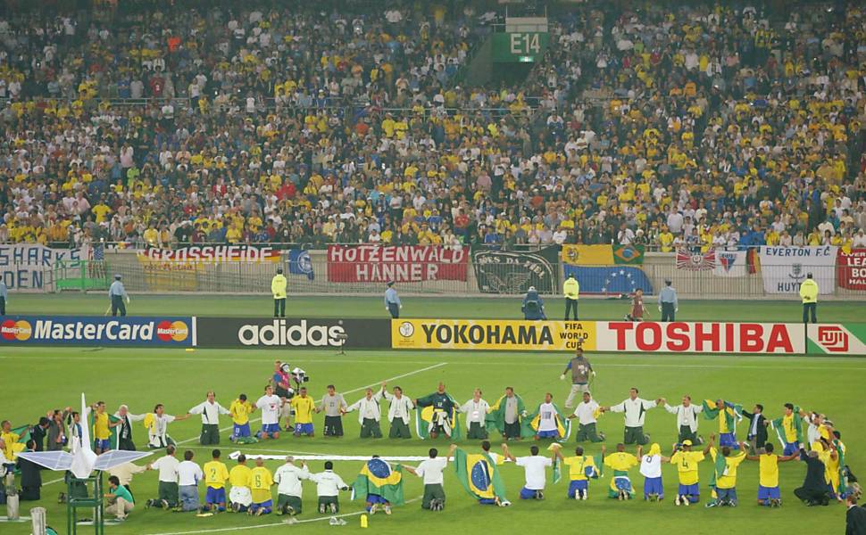 Membros da comissão técnica e jogadores, alguns cobertos com bandeiras do Brasil, se ajoelham e rezam no gramado após conquista do título do pentacampeonato