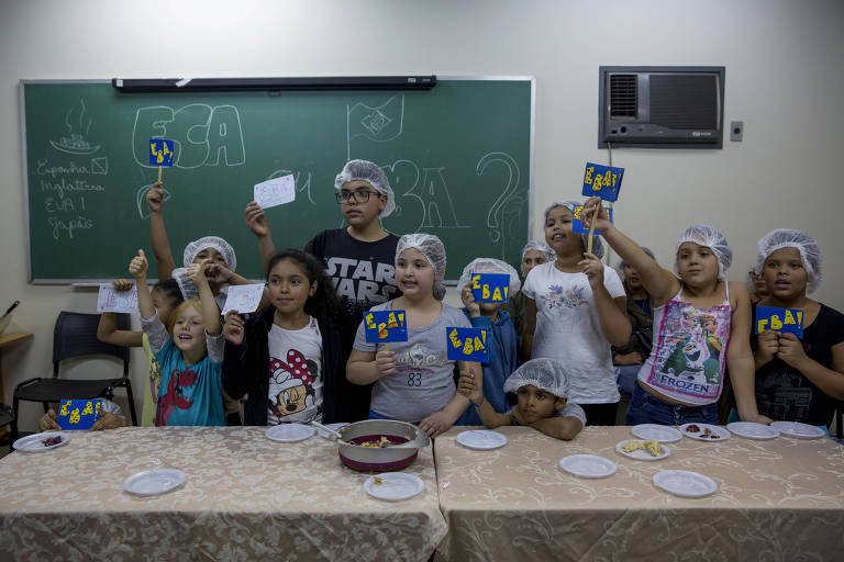 Crianças no Centro de Recuperação e Educação Nutricional, depois de comerem um bolo feito com frutas, seguram placas que dizem Eba