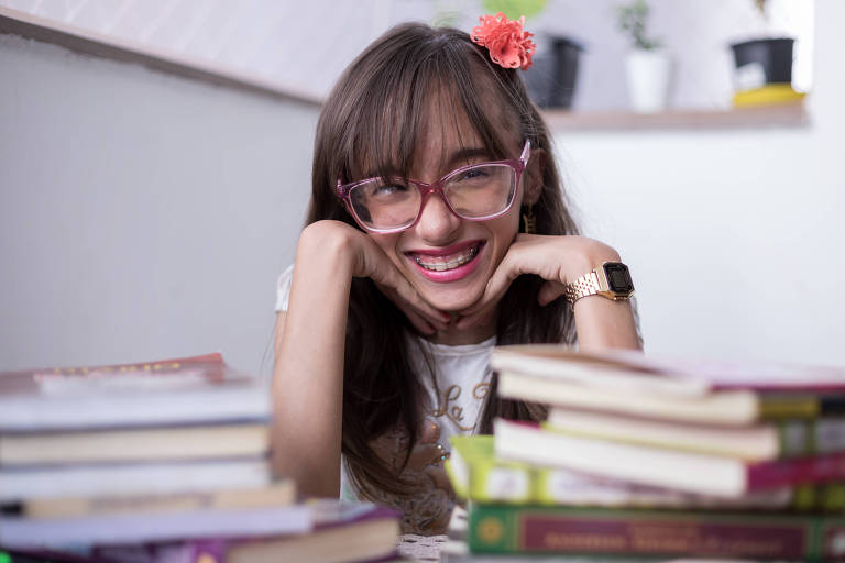 A estudante Heloíza Carmona Santos, de 14 anos, em frente a livros. Ela foi diagnosticada com hidrocefalia grave quando nasceu e passou por três cirurgias complicadas no cérebro. Agora, escreveu um livro