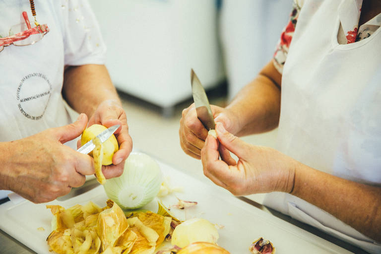 Arroz com lentilha
(receita usada nos dias em que a proteína não vem da carne)
Frite bastante cebola, acrescente arroz integral, lentilha crua, sal, água fervente e deixe cozinhar

Cuscuz de sardinha
250g de sardinha, 100 g de farinha de milho flocada (na merenda, a chef aproveita também corn flakes que é distribuído para as escolas), alho, cebola, salsão picado, salsinha e cebolinha.
Hidrate a farinha ou o corn flakes em água e sal, por cerca de 10 minutos. Refogue a cebola e alho, coloque a sardinha e os temperos e cozinhe até que a massa fique com ponto de brigadeiro. Pode ser servido quente ou frio. (na foto, merendeiras descascam batatas)