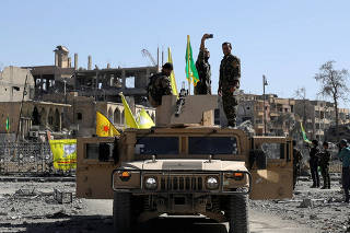 A Fighter of Syrian Democratic Forces takes a selfie as he stands on a military vehicle in Raqqa