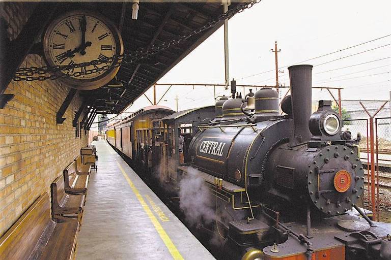 O trem está parado em uma estação com cara de antiga, em São Paulo. É mostrada a plataforma vazia, e um relógio de ponteiro clássico, com moldura de metal, está suspenso no teto.