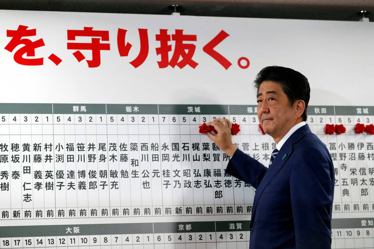 Japan's PM and LDP leader Abe looks on as he puts a rosette on the name of a candidate who is expected to win the lower house election at the LDP headquarters in Tokyo