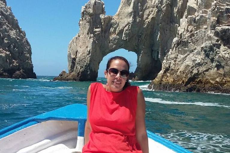 Marcela posa em um barco no meio do mar. H rochas ao fundo, e o cu est bastante azul