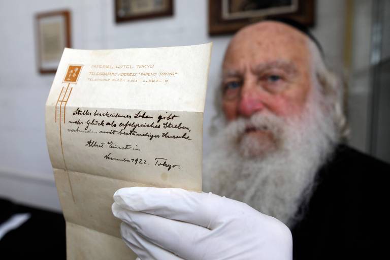 (FILES) This file photo taken on October 19, 2017 shows an Ultra-Orthodox Jewish man displaying one of two notes written by Albert Einstein, in 1922, on hotel stationary from the Imperial Hotel in Tokyo Japan, at the Winner's auction house in Jerusalem. The note that Albert Einstein gave to a courier in Tokyo briefly describing his theory on happy living sold at auction in Jerusalem on October 24, 2017 for $1.56 million, the auction house said. / AFP PHOTO / MENAHEM KAHANA ORG XMIT: 663