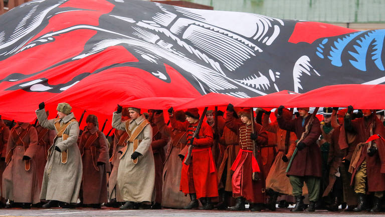 Participantes vestidos com uniformes históricos carregam uma bandeira gigante enquanto participam de um desfile militar na Praça Vermelha em Moscou, Rússia