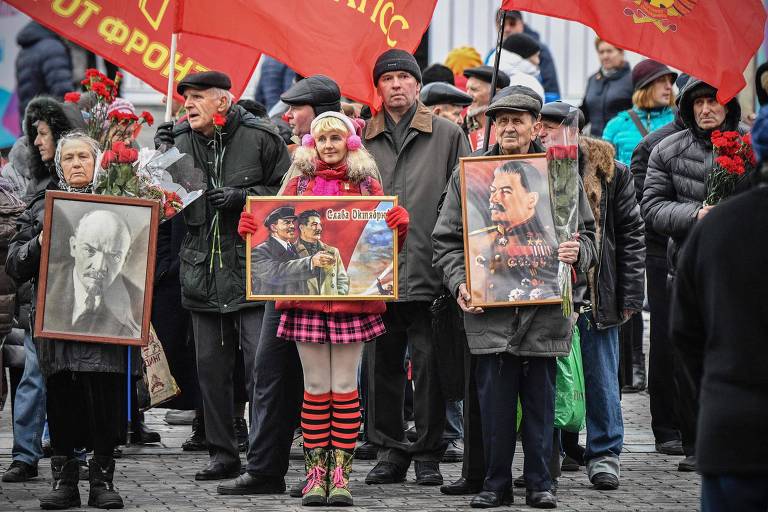 Partidários comunistas russos agitam bandeiras e seguram cartazes na entrada da Praça Vermelha, em Moscou, para lançar flores no mausoléu de Lenin, comemorando o próximo 100º aniversário da Revolução Bolchevique