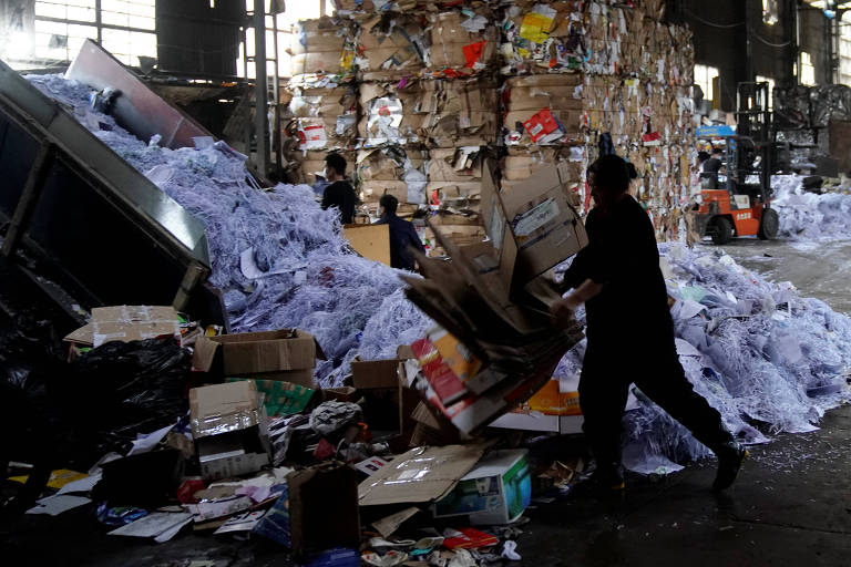 Trabalhadores em local com pilhas de papelão e esteiras de onde caem folhas de papel