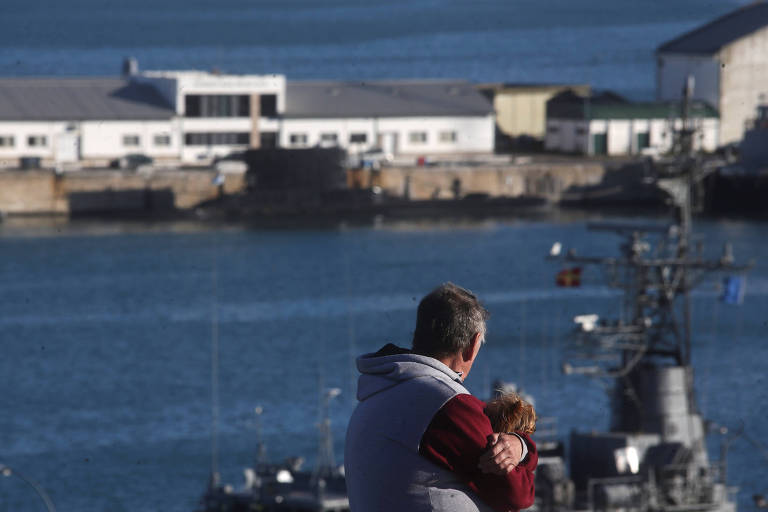 Um homem segura um cachorro enquanto olha para navios na base naval, onde o submarino ARA San Juan desapareu, em Mar del Plata