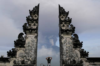 A tourist watches as Mount Agung volcano erupts at Lempuyang Temple in Karangasem, Bali