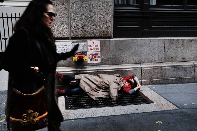 Mulher passa em frente a sem-teto em rua de Manhattan; hotis em bairros nobres viram abrigos