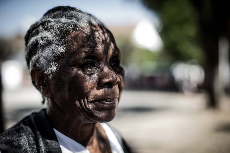 Imagem mostra mulher negra de cabelos grisalhos. Ela está de lado em uma praça.