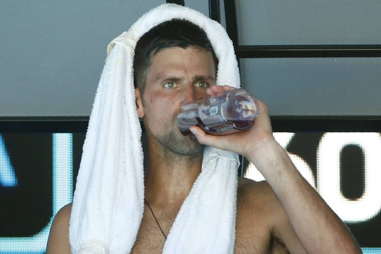 Novak Djokovic, sem camiseta e com uma toalha na cabeça, toma água