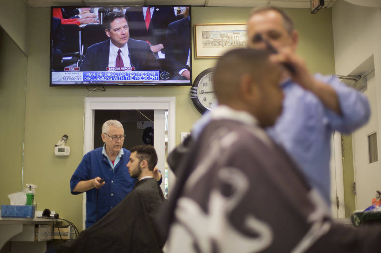 Barbeiros trabalham enquanto a TV exibe o testemunho de James Comey, diretor do FBI, em junho de 2017