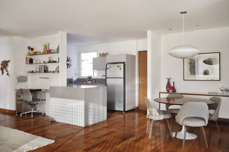 Nesse projeto feito pelo escritório RAP Arquitetura e Interiores, uma parte da cozinha virou a área de trabalho de um apartamento de 135 metros quadrados na Vila Madalena (zona oeste da capital). Os dois ambientes são separados por um painel de madeira MDF pintado de branco. A mesa foi feita com madeira pau-ferro. Em cima, foram instaladas prateleiras de aço corten. “Fizemos tudo bem fino para ganhar o máximo de espaço possível”, explica a designer Ana Veirano.