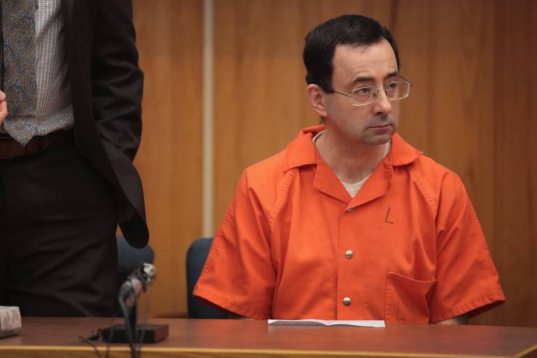 O médico Larry Nassar, de roupa laranja, triste enquanto escuta sua sentença
