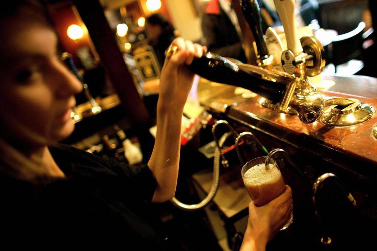 Bartender tira um pint de cerveja em um pub no centro de Londres; cidade lança 'bolacha' para verificar colarinho