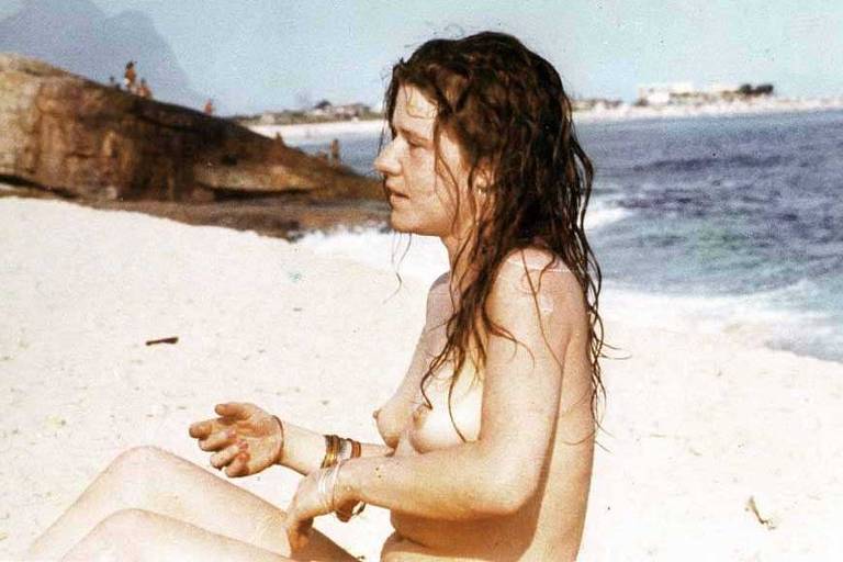 A cantora Janis Joplin sentada na praia no Rio de Janeiro, de topless