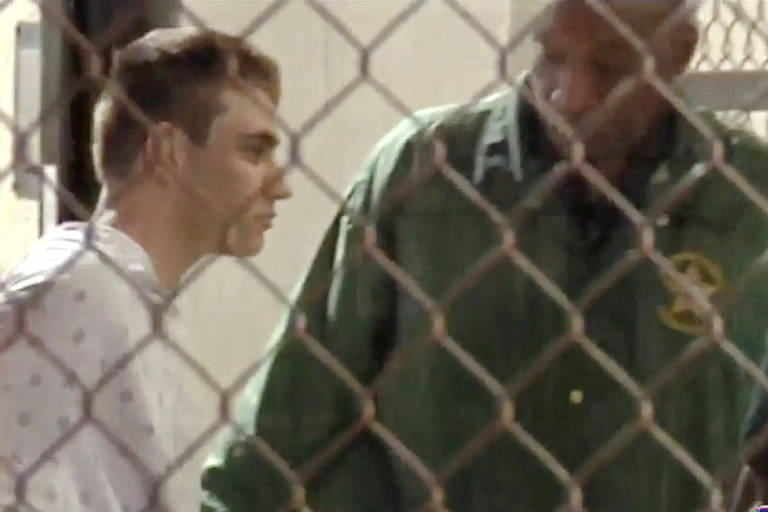 Imagem de TV mostra Nikolas Cruz (esq.) chegando à prisão escoltado por um policial no condado de Broward