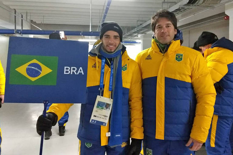 O atleta Victor Santos segura uma placa com a bandeira do Brasil ao lado do treinador Leandro Ribela